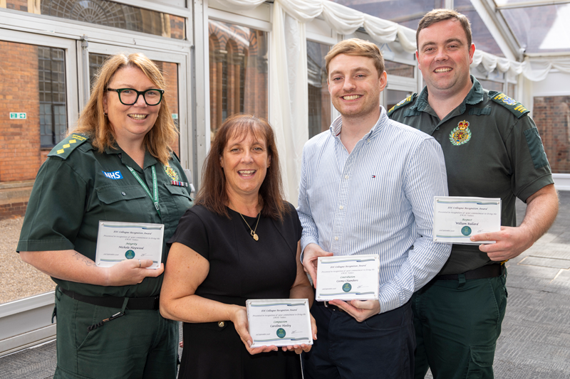 Four East Midlands Ambulance Service colleagues pose for a photograph while holding EMAS Values Awards certificates. The group stands indoors at an awards event with their certificates displayed towards the camera.