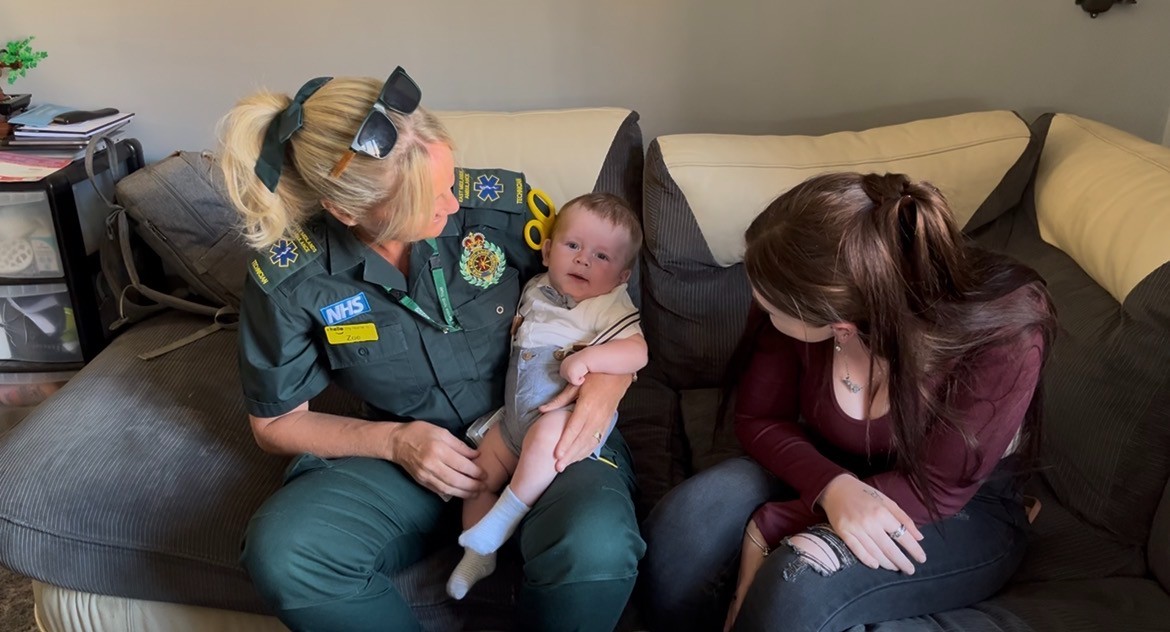 Zoe Spilsbury in green EMAS uniform gets to hold baby Oscar as Elli looks on at the moment.