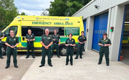 A group of people in green ambulance uniform, including Brian Jaffrey, are seen standing in front of an EMAS ambulance