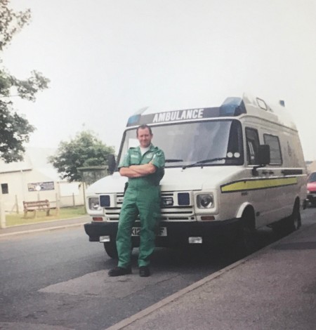 Brian Jaffrey in a green ambulance uniform stands beside an ambulance. The picture was taken in 1992 up in Scotland.