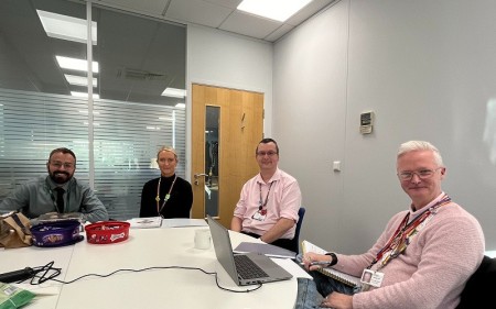 A scene of four people sitting around a table, including the assessor of the rainbow accreditation along with members from our Health, Wellbeing and Inclusion team.
